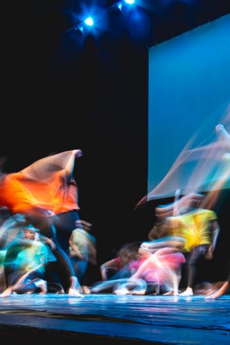 Group of dancers in coloured clothes dancing on the stage in long exposure