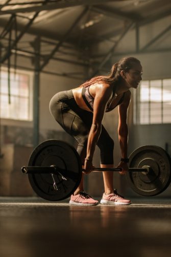 Fit young female athlete lifting heavy weights. Fitness model performing weight lifting exercise at gym.