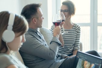 Sad little child listening to music alone while addicted parents drinking alcohol at home. Family Alcoholism problem