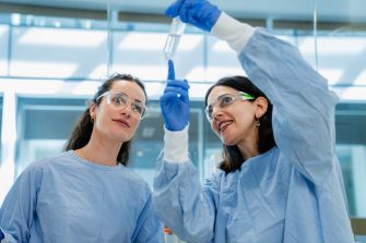 Two women in lab coats holding a vial.