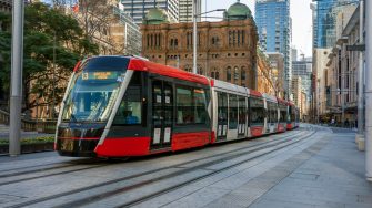 Red tram, light rail on empty city street, Sydney, Australia