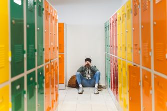 Sad pensive teenager sitting alone in the floor in locker room.