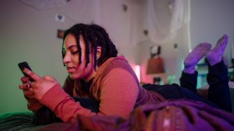 Young woman types on her phone in bed