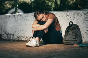 Woman, student and depression in lonely stress, anxiety or mental health problems in the outdoors. Sad and depressed female teenager in distress, loneliness or trouble at school or university.
