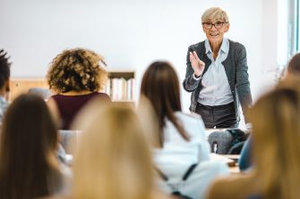 Happy senior teacher talking to large group of univerity students in amphitheater