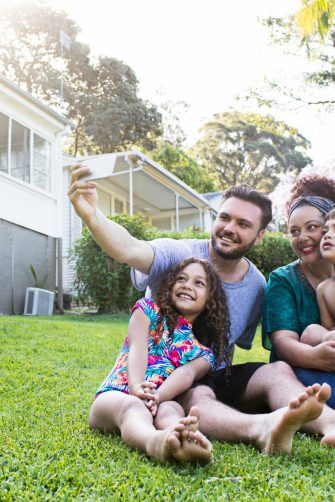 Aboriginal Family portrait with 1 parent and 2 children. They are sitting on the front porch. Everyone is happy and smiling. Could be a single mother.