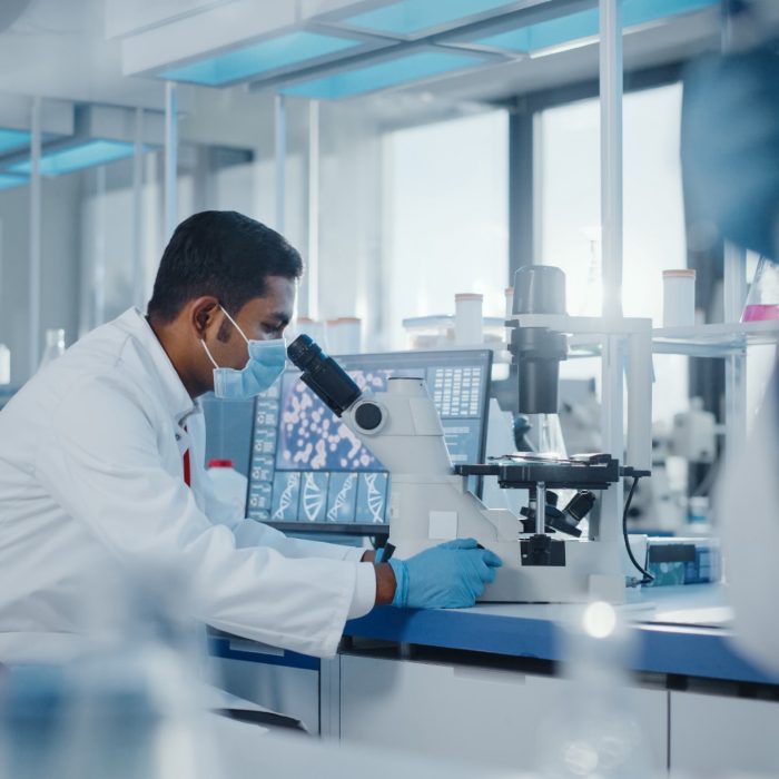 Indian male scientist looking under microscope in lab