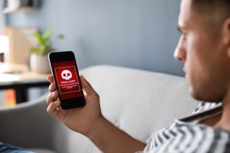 Man holding smartphone with warning about virus attack at home, closeup