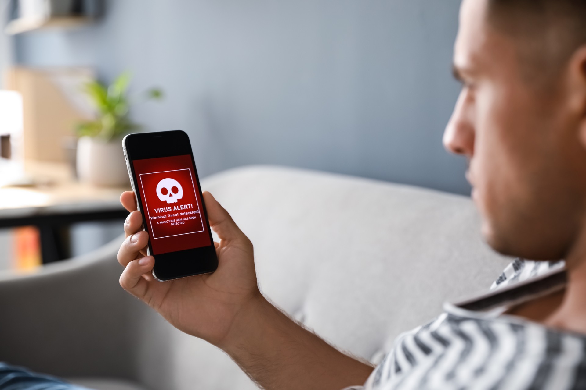 Man holding smartphone with warning about virus attack at home, closeup