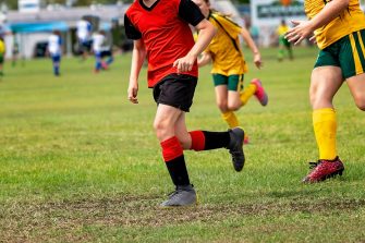 An action of shot of young boys playing rugby. One boy is leaning into a tackle with the ball tucked under his arm.