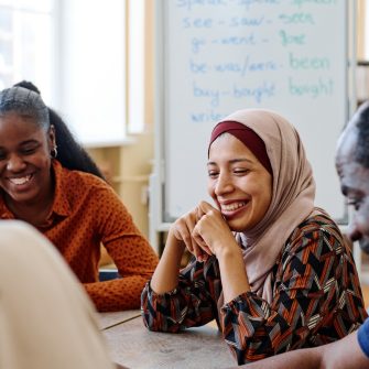 Group of modern immigrants sitting at table having fun laughing at something funny during english lesson