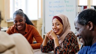 Group of modern immigrants sitting at table having fun laughing at something funny during english lesson