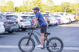 A man in a blue shirt and black helmet rides his e-bike past cars