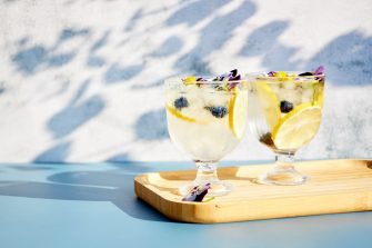 Chilled cocktails with fresh citrus fruits garnished with edible flowers on a wooden serving board. Summer drinks with soda and fruit.
