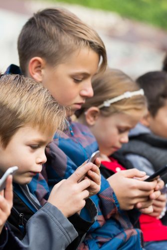 Outdoor portrait of little girls and boys playing with phones 