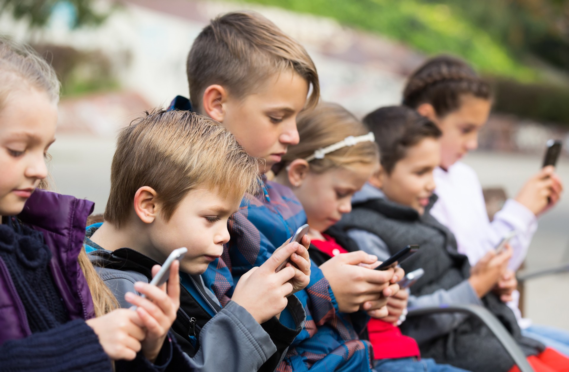 Outdoor portrait of little girls and boys playing with phones 