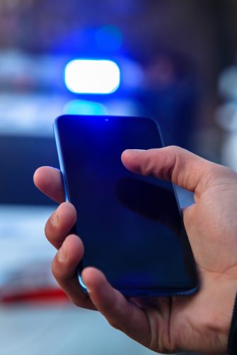 man holding phone with police in street