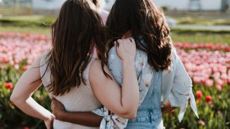 Two young women hold each other while looking into field of red tulips