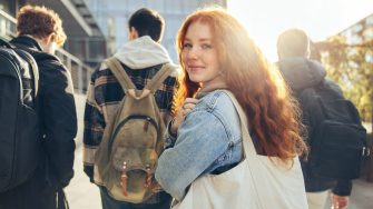 Female student glancing back while going for a class in college. Girl walking with friends going for class in high school.