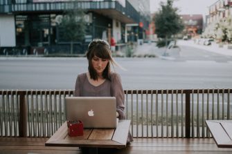 Young woman sitting at outdoor cafe table with laptop