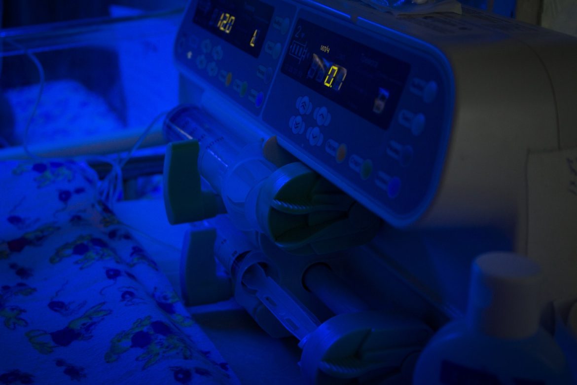 Newborn baby under blue UV light for phototheraphy on infant warmer in neonatal intensive care unit. Child baby having a treatment for jaundice under ultraviolet light in incubator. Device for delivery of a dropper.