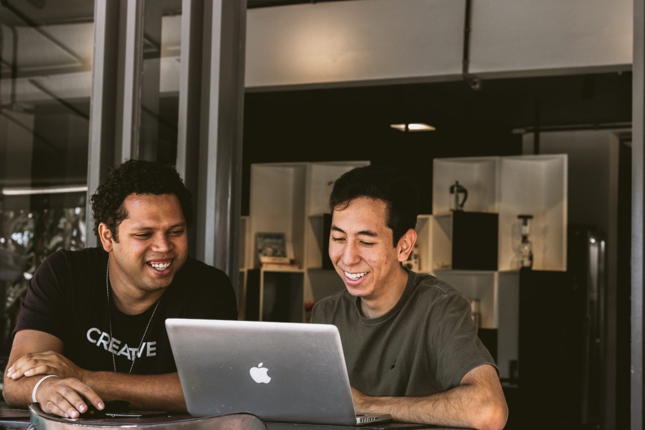 Two smiling men looking at Macbook