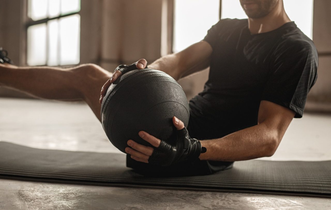 Side view of an athletic male doing side twist exercise with medicine ball during intense training in gym
