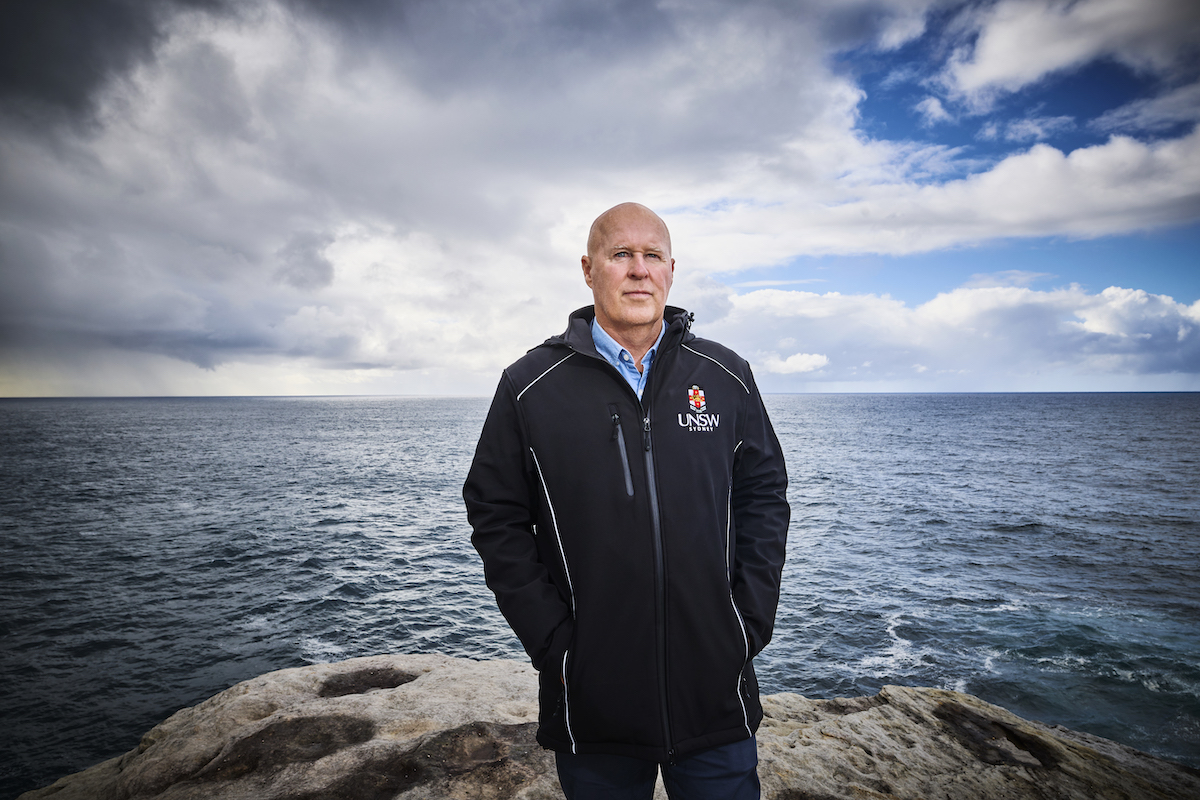 Photo of Professor Matthew England standing on a clifftop with the ocean in the background