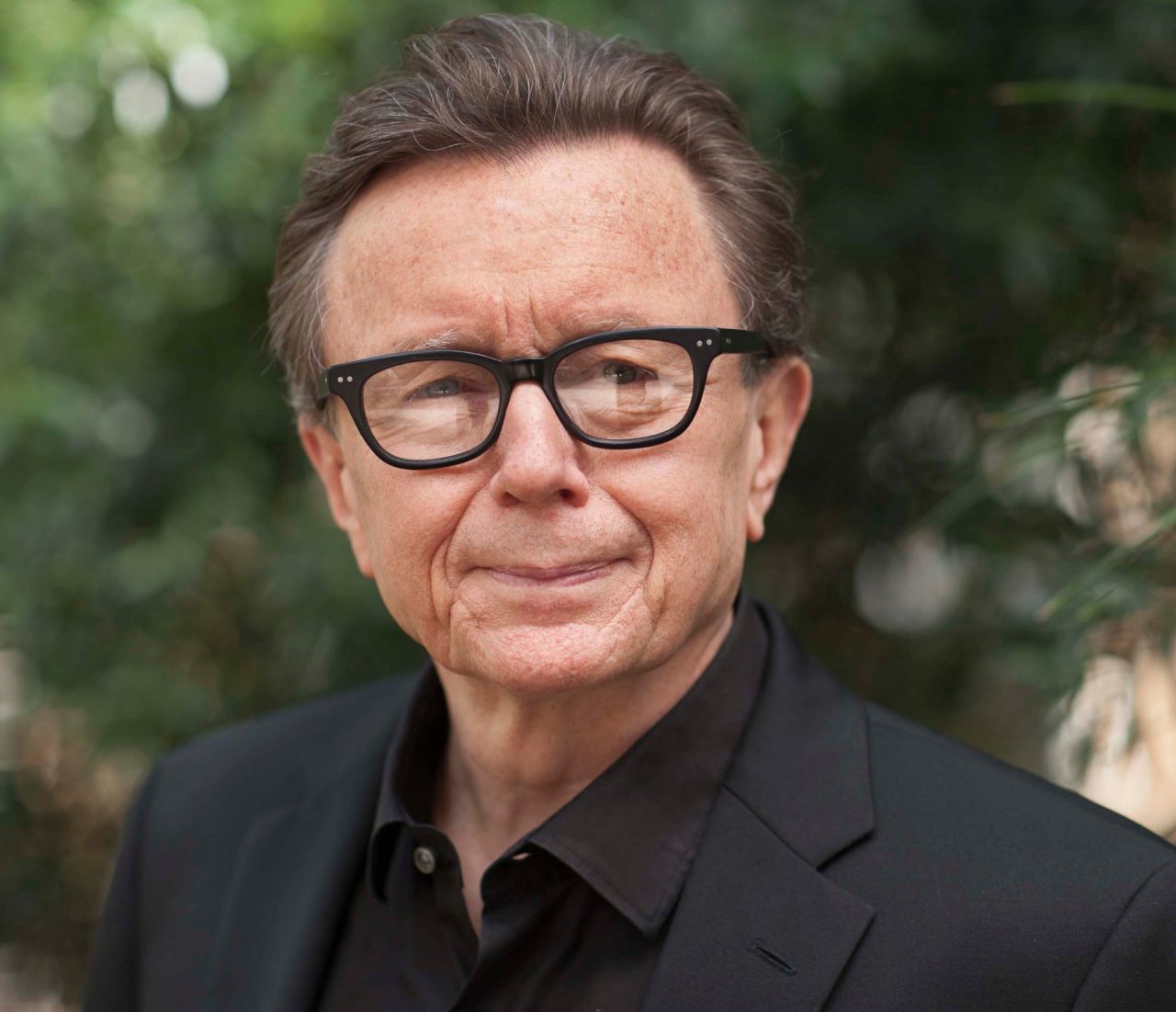 A man with black glasses in a black suit.